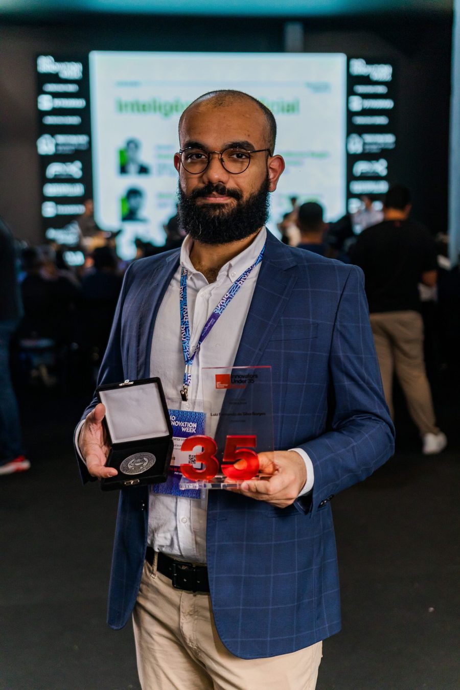 Luiz Fernando da Silva Borges segura o troféu Innovators Under 35 da MIT Technology Review e uma medalha, em um evento